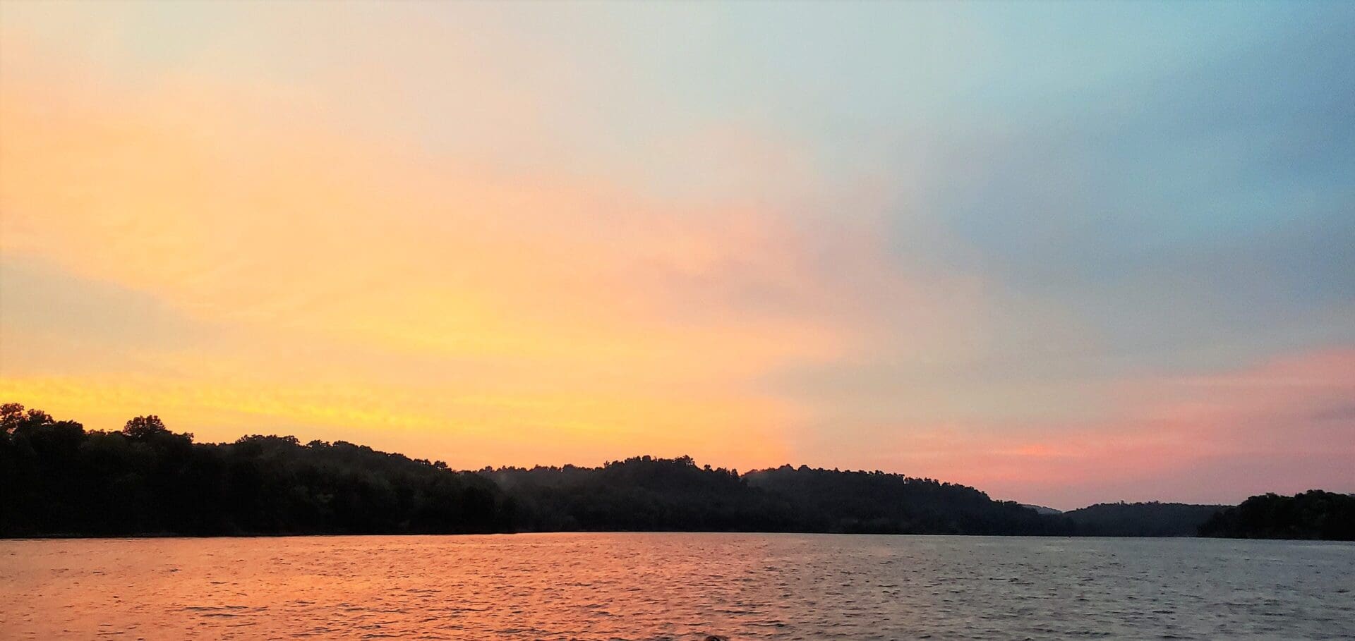 Sunset over a calm lake with silhouetted trees.