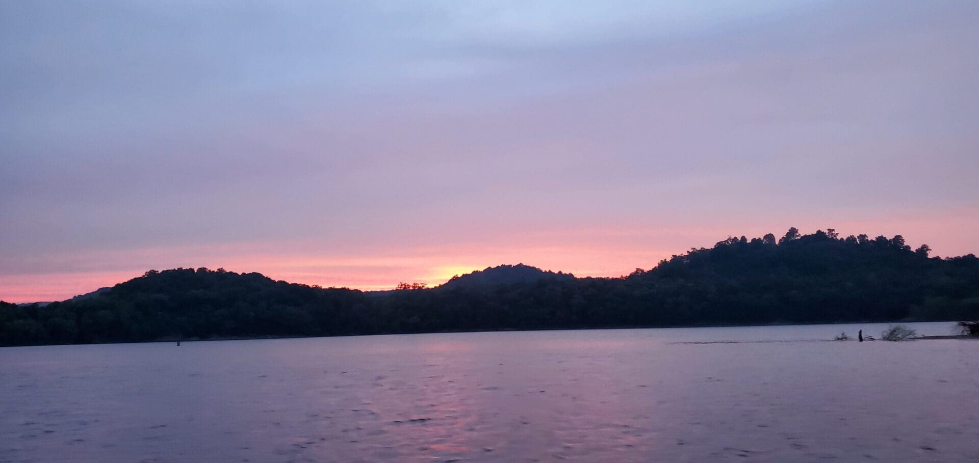 Sunset over calm water with silhouetted hills.