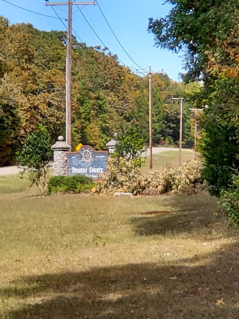 A sunny park area with a sign and trees in the background.