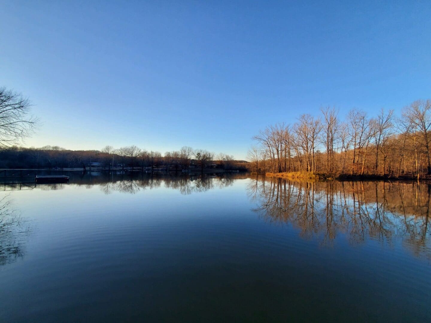 A calm lake reflecting a clear blue sky with trees on the shore.