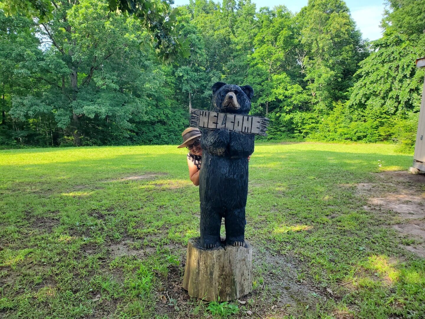 A wooden bear statue holding a sign in a green park.