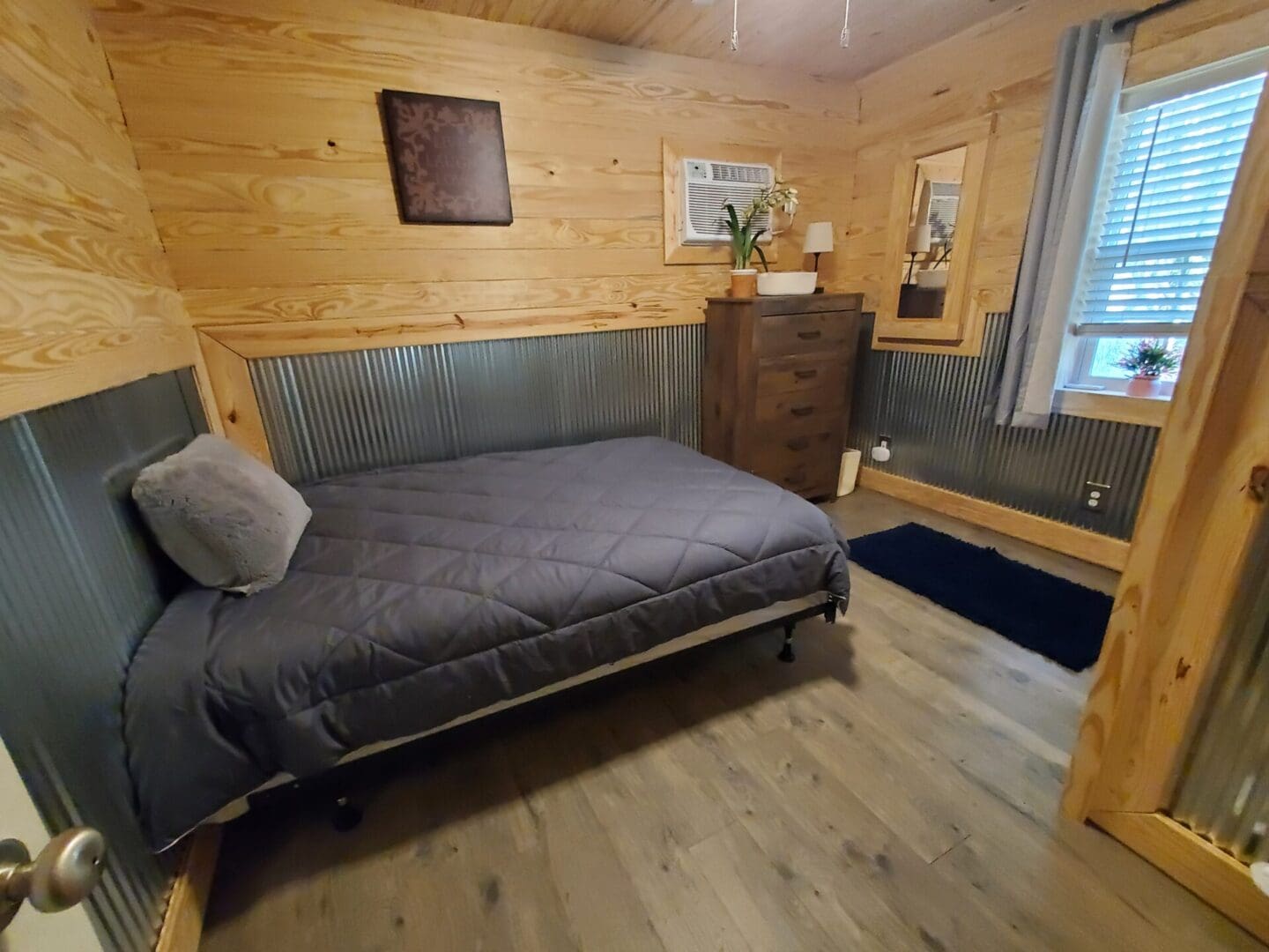 Cozy wooden room with a dark gray sofa bed and chest of drawers.