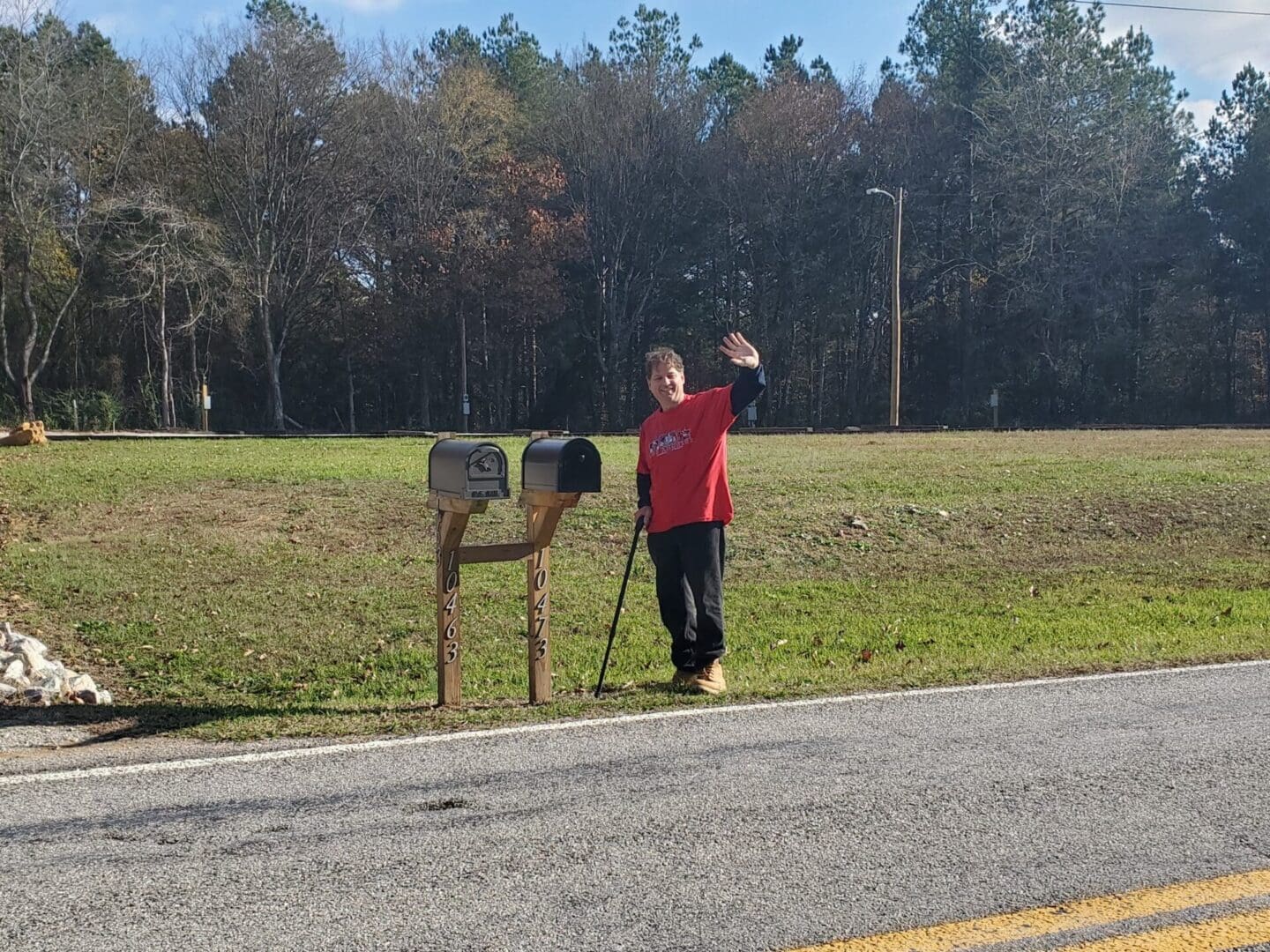 A person in a red shirt waving beside mailboxes on a rural road.