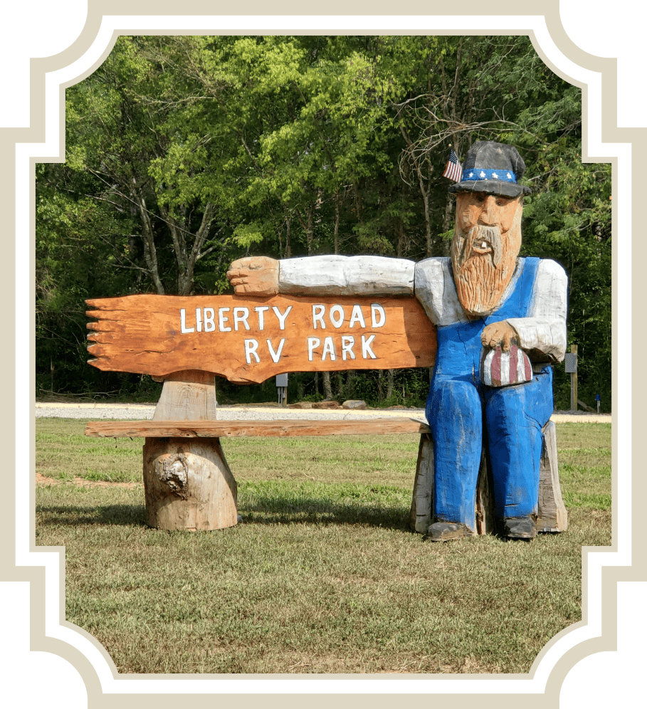 Wooden statue of a man holding a Liberty Road RV Park sign.