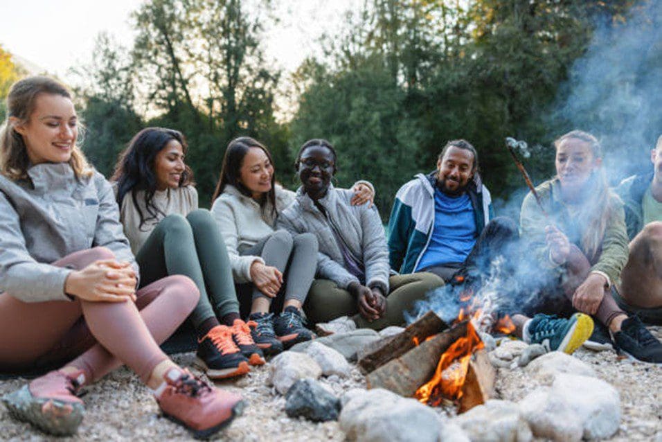 A group of friends sitting around a campfire outdoors, sharing laughter.