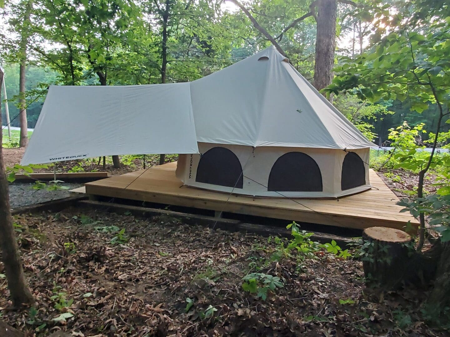 A large white tent with arched windows on a wooden platform in a wooded area.