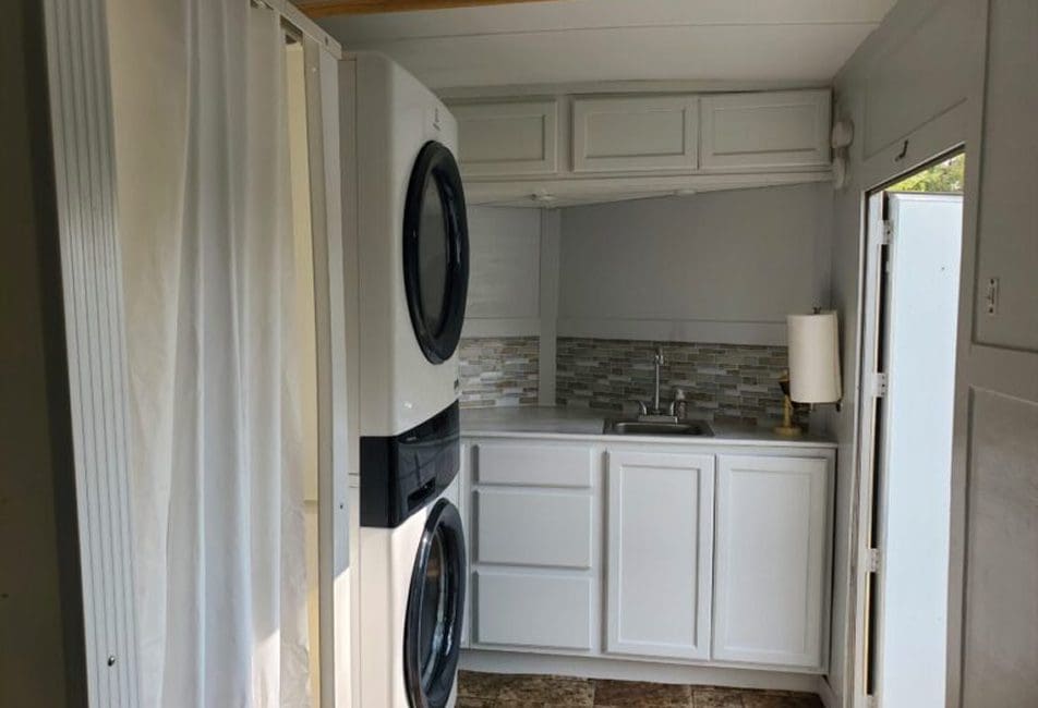 Compact laundry area with stacked washer and dryer beside white cabinets.