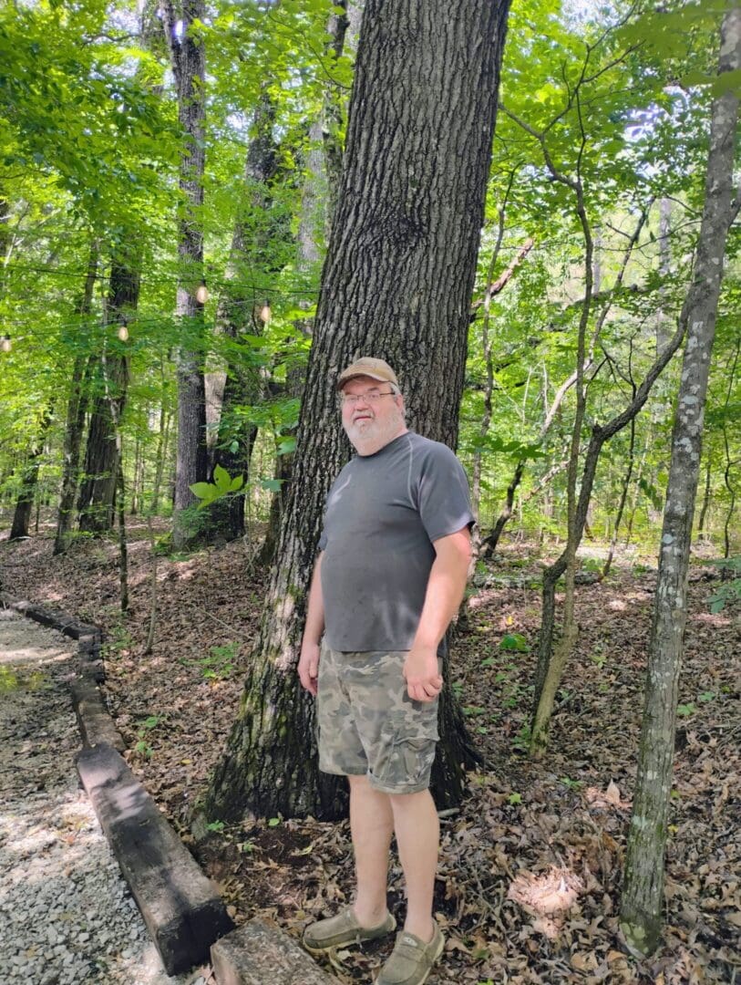 A man standing in a forest near a tree.