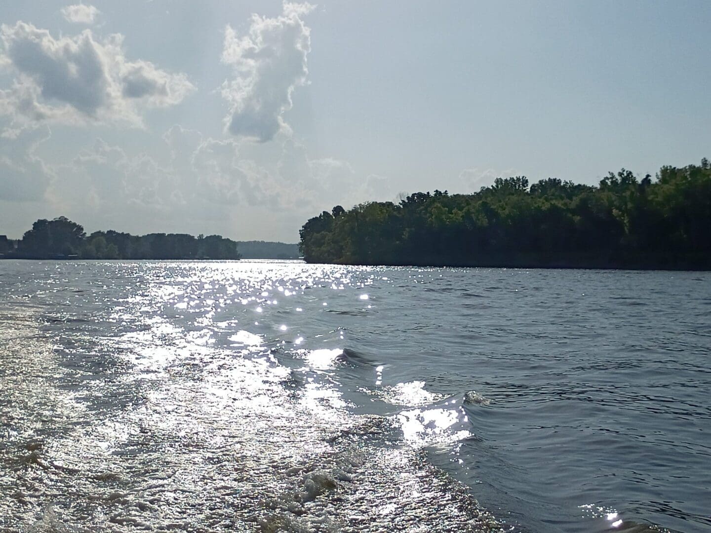 Sunlit river with trees and clouds.