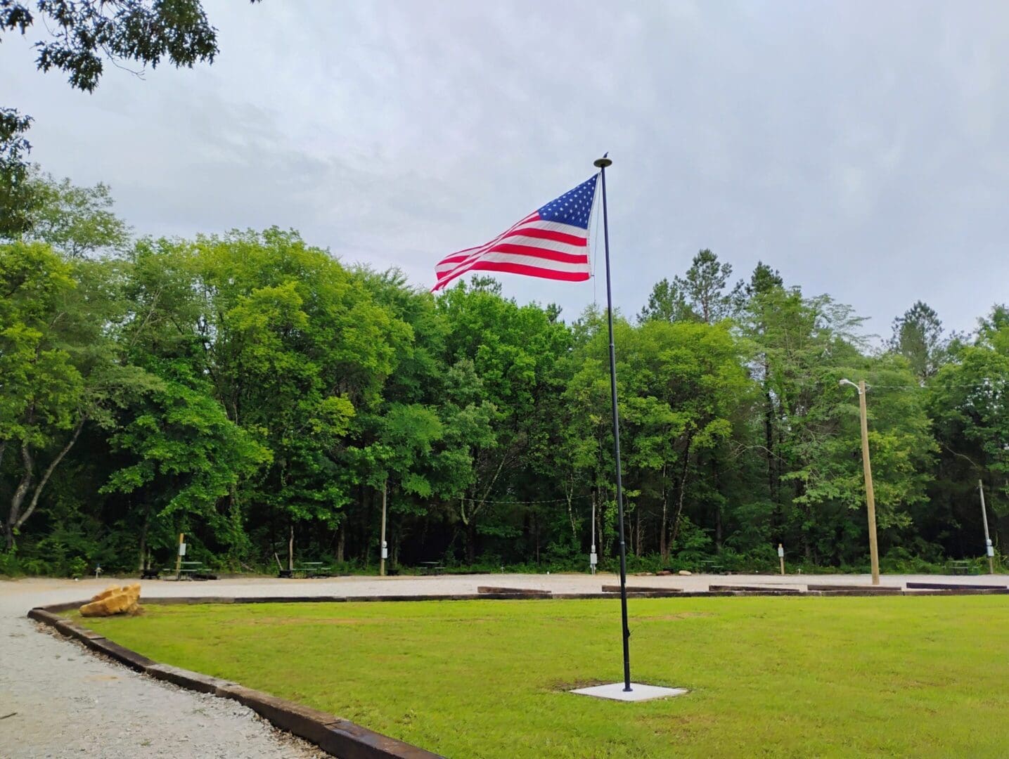 An American flag waving on a pole near a green forest.