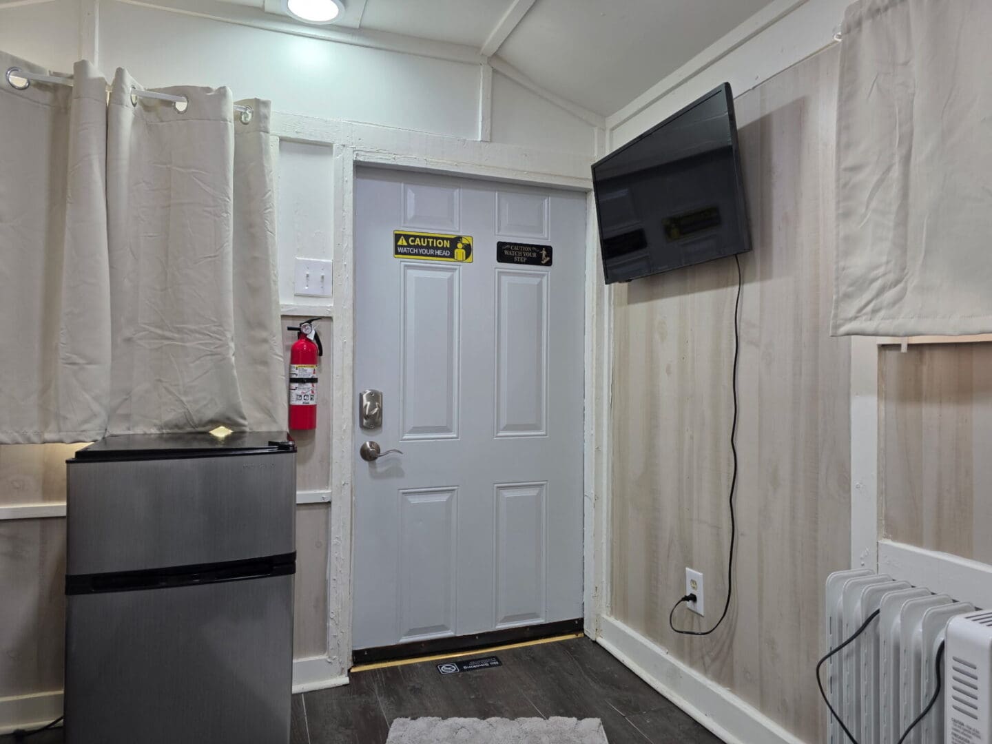 Small room with door, fridge, wall TV