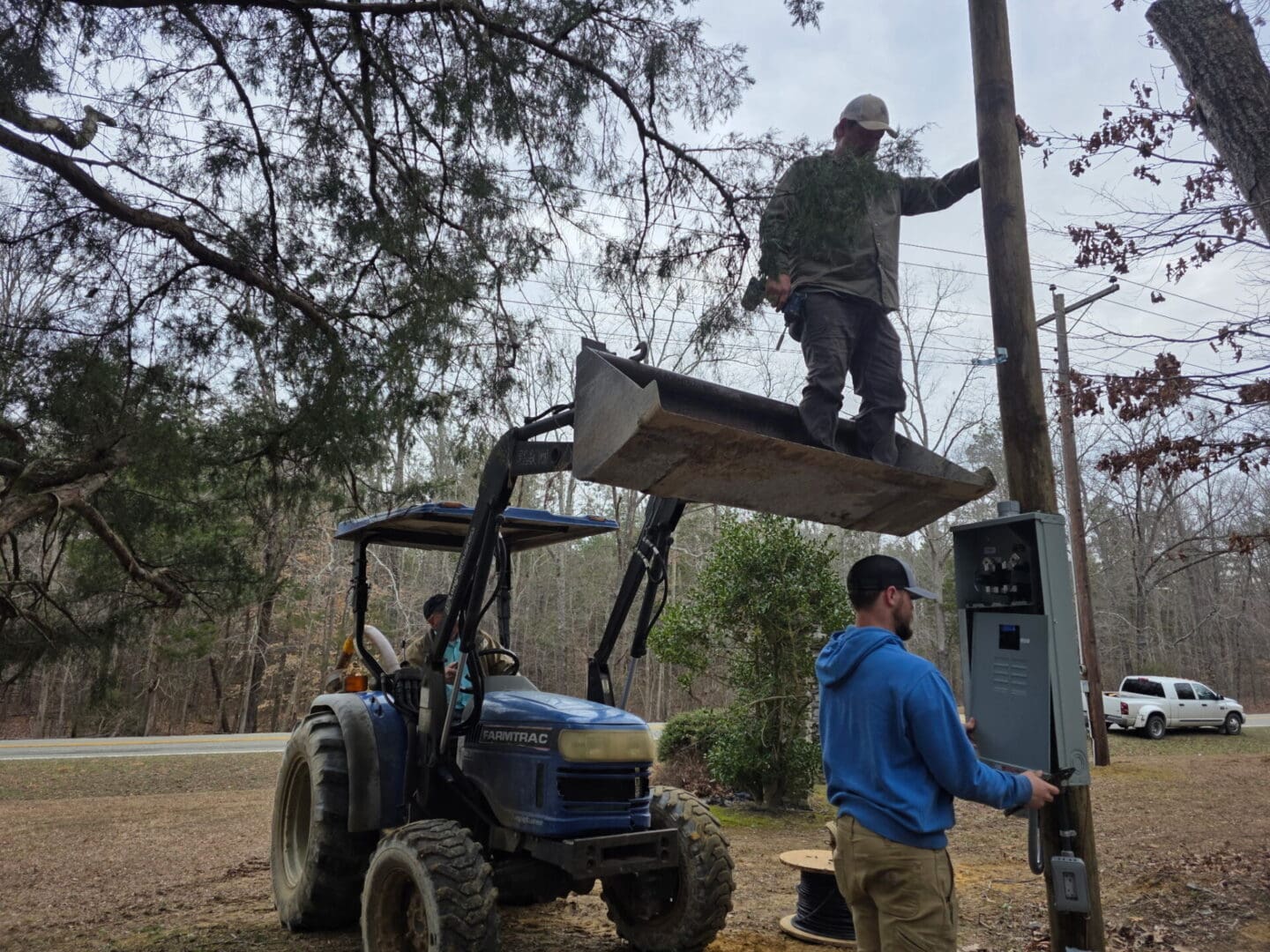 Two workers installing electrical panel using tractor