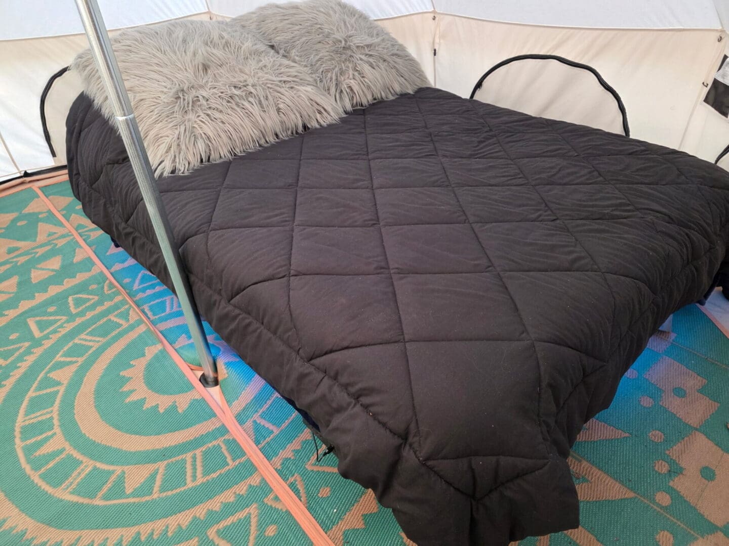 Bed with black quilt and furry pillows
