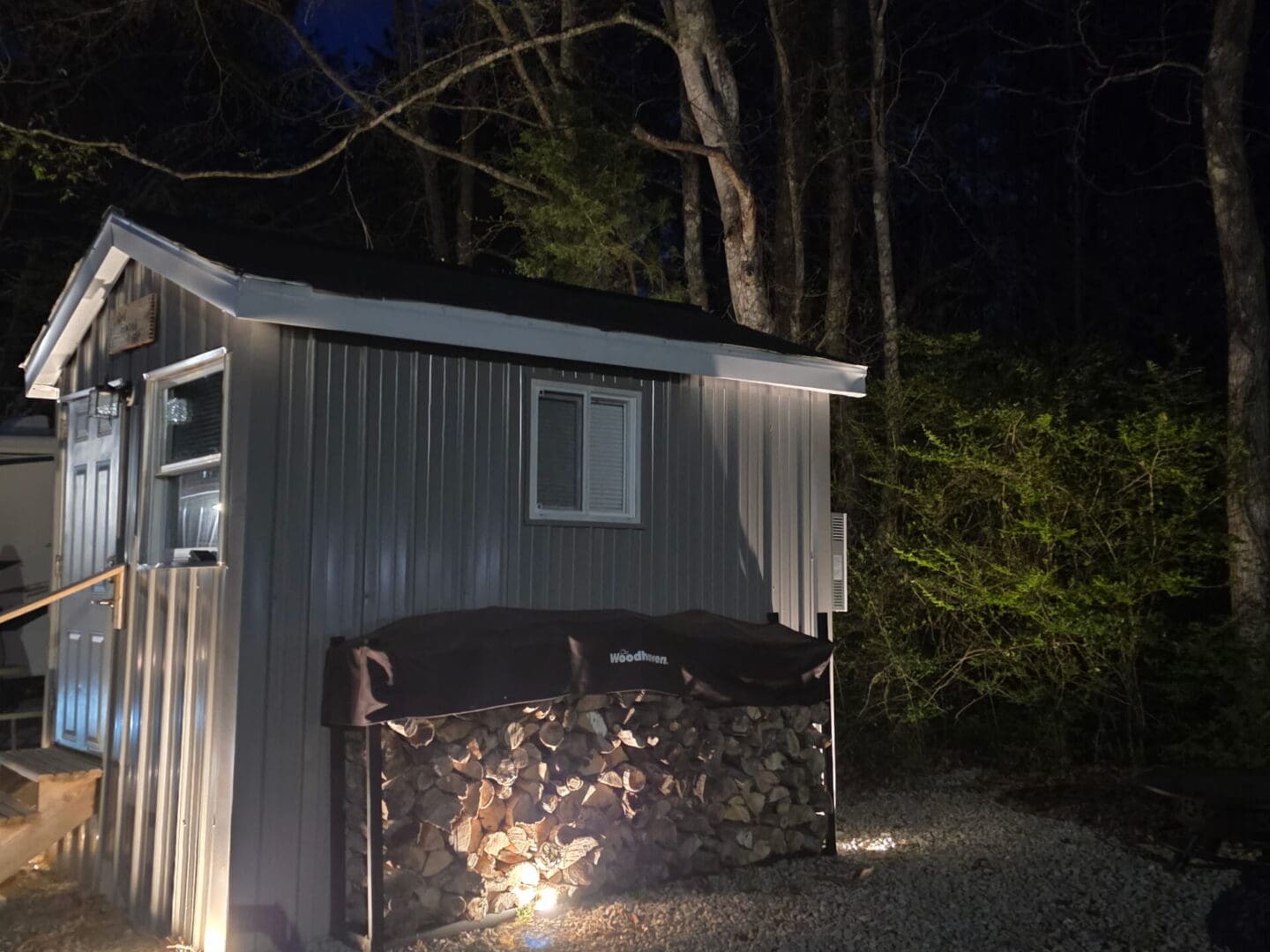 Small lit metal shed with stacked firewood