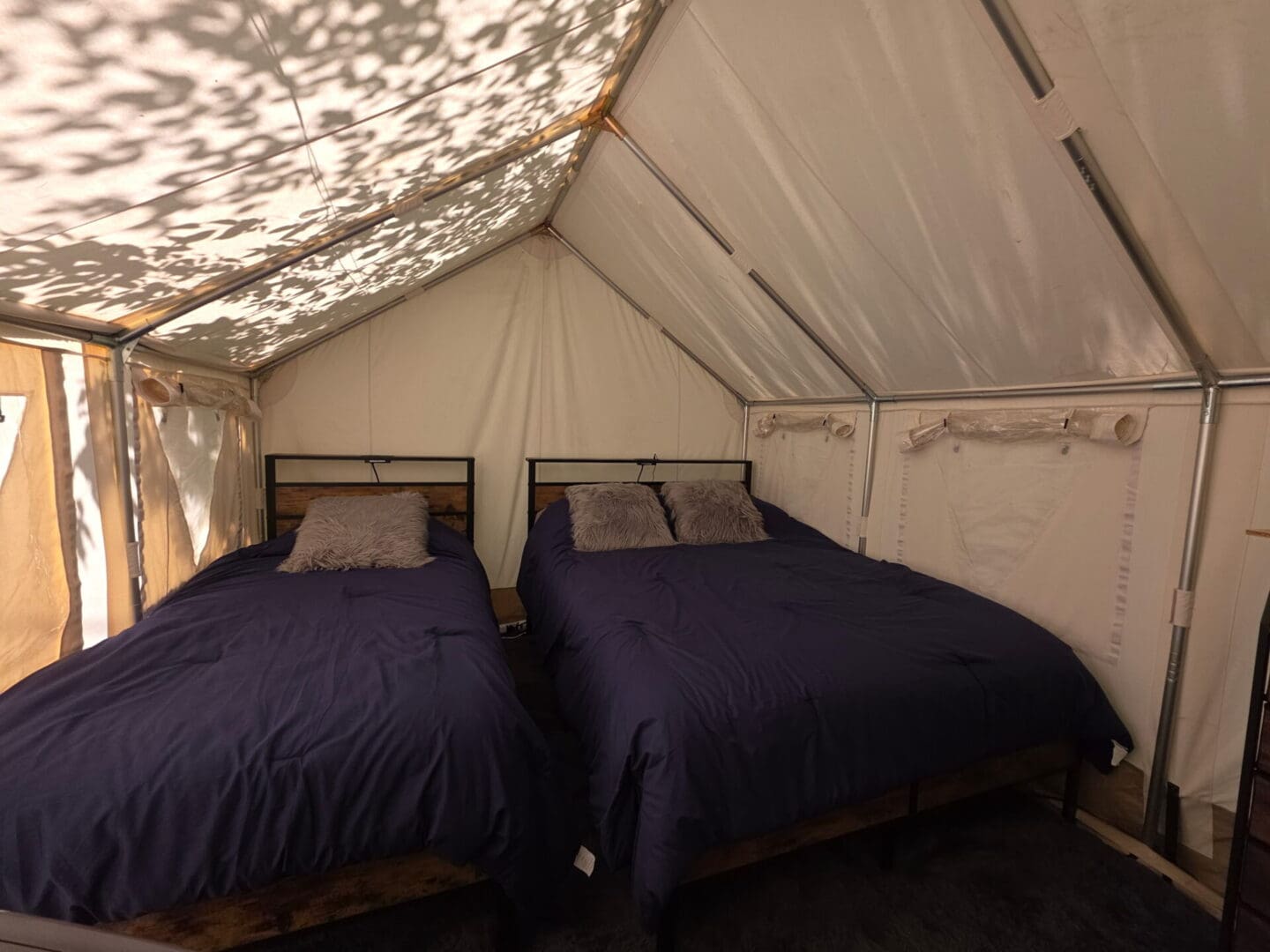Two beds in canvas tent with leaf shadows